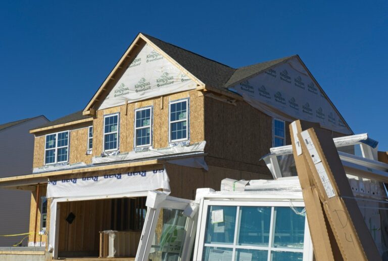 A house under construction with plywood walls and stacked windows in the foreground